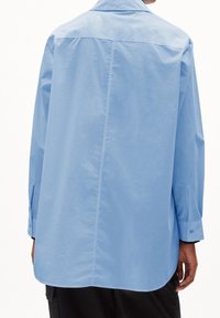 Light blue shirt with a button-down collar, long sleeves, and a curved hem. Made of smooth fabric with a slightly glossy texture.