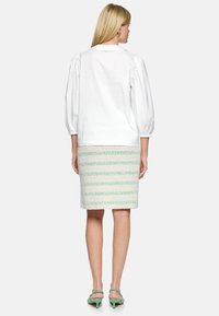 White shirt with puffed sleeves paired with a textured pencil skirt featuring green and white stripes. Green heels complete the look.