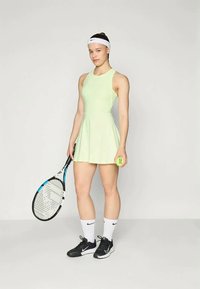 Tennisikleid heledast rohelisest kangast, flared seeliku ja mustade tennistega; valgete pahkl sockside ja tennisepalli ning reketiga.
