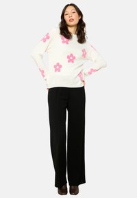 White sweater with pink flower patterns, paired with black wide-leg pants. The sweater features a round neckline and loose fit.