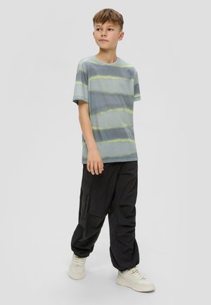 Camiseta gris con rayas amarillas, escote redondo, combinada con pantalones cargo negros y zapatillas de color claro. Atuendo casual de estilo urbano.
