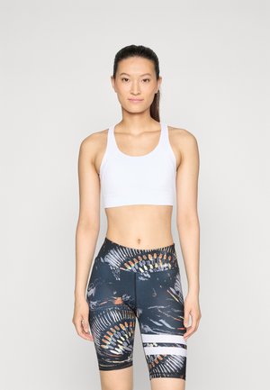 White athletic crop top with wide straps paired with high-waisted, black shorts featuring colorful abstract patterns and white horizontal stripes.