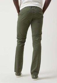 Pantalones de algodón color verde oliva con un diseño de pierna recta, que presentan bolsillos traseros y una textura suave. Combinados con zapatillas blancas.