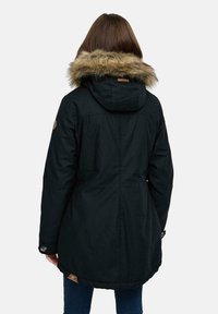 Svart parka-jacka med en huva fodrad med päls, lång silhuett, sidfickor och en läderlogotyp på nederkant. Slät, strukturerad tyg.