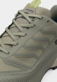 Αδιάβροχο αθλητικό παπούτσι σε ανοιχτό πράσινο χρώμα Scarpa με υφή στην σόλα, συνθετικό πάνω μέρος με σχέδια και κορδόνια ταιριαστού χρώματος που περνούν μέσα από πέντε οπές.