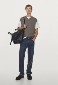 Gray sleeveless sweater over a white t-shirt, blue jeans, and black sneakers. Holding a large black leather tote bag with straps.