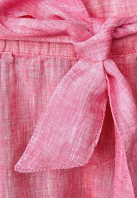 Růžová lněná látka se svařeným detailem mašle, která má jemnou texturu a subtilní lesk. Látka vypadá mírně průsvitně s tkaným vzorem.