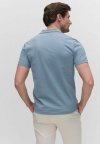 Pikétröja i ljusblå bomull med korta ärmar, krage och en slät yta, i kombination med ljusbeiga byxor.