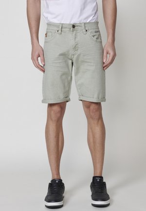 Lichtgroene denim short met opgerolde uiteinden, voorzien van zijzakken en een logo label. Gekocht met zwarte sneakers en een wit t-shirt.