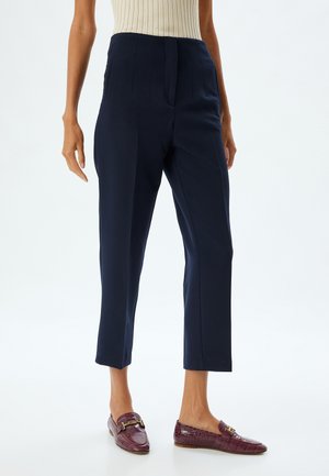 Pantalones de marina ajustados con pliegues frontales y bolsillos laterales, con un corte recortado. Llevados con mocasines decorativos en burdeos.
