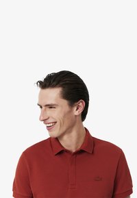 Röd kortärmad polo med en texturerad tyg, med en klassisk krage och en broderad logotyp på bröstet.