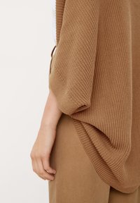 Bruin gebreid top met een gestructureerde afwerking, voorzien van verlaagde mouwen, gecombineerd met bijpassende bruine broek. Zachte, ontspannen pasvorm en gedrapeerde silhouet.