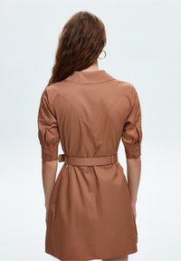 Robe brune à manches courtes, avec une taille cintrée, un col et des poignets boutonnés. Fabriquée en tissu lisse, elle présente un design ceinturé et des détails de couture au dos.