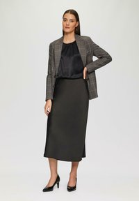 Schwarze Satinbluse mit plissiertem Ausschnitt, grauer Karoblazer und glatter schwarzer Rock. Akzentuiert mit schwarzen High Heels. Minimalistisches Design.