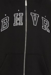 Felpa con zip nera caratterizzata da audace scritta bianca "B H V R" con un carattere sportivo. Include tasche frontali e una chiusura con cerniera liscia.