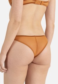 String brun en dentelle avec un bord contrastant brun. Présente une texture lisse, une couverture minimale et un design sans coutures sur les bords.