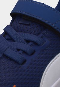 Κοντινό πλάνο μπλε αθλητικού παπουτσιού με διχτυωτό ύφασμα, υφασμένες κορδόνια, λουράκι με βέλκρο και λευκή λαστιχένια σόλα.