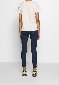 Světle růžové bavlněné tričko, tmavě modré skinny džíny a multicolor tenisky s černými akcenty a texturovanou podrážkou. Jednoduchý design, žádné grafiky.