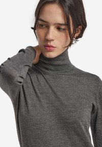 Grå rullkragströja i mjukt material, med långa ärmar och rynkdetaljer vid ärmsluten. Slät textur och figurnära design.