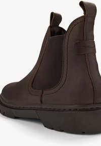 Bottines en cuir marron avec panneaux élastiques sur les côtés, semelle en caoutchouc texturée et détails de couture. Équipées de tirants pour un enfilage facile.