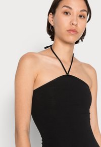 Top halter preto, design ajustado, textura em nervuras, laços finos no pescoço, estilo minimalista, bordas sem costura, usado por uma modelo com cabelo curto.