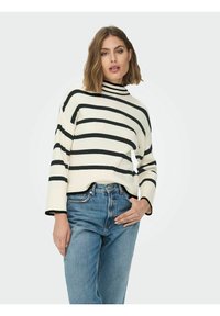 Prugasti džemper s rolkom u krem i crnoj boji, rebraste teksture, s dugim rukavima i opuštenim krojem, uparen s trapericama visokog struka modre boje.