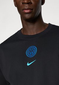 Sort bomulds t-shirt med blåt Inter Milan logo og turkis Nike swoosh. Crew neck design med en blød tekstur.