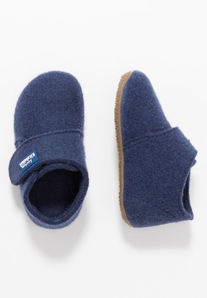 Paire de chaussons en laine bleue avec semelles en caoutchouc marron, l'un montre le dessus avec une bride réglable, l'autre la vue de côté.