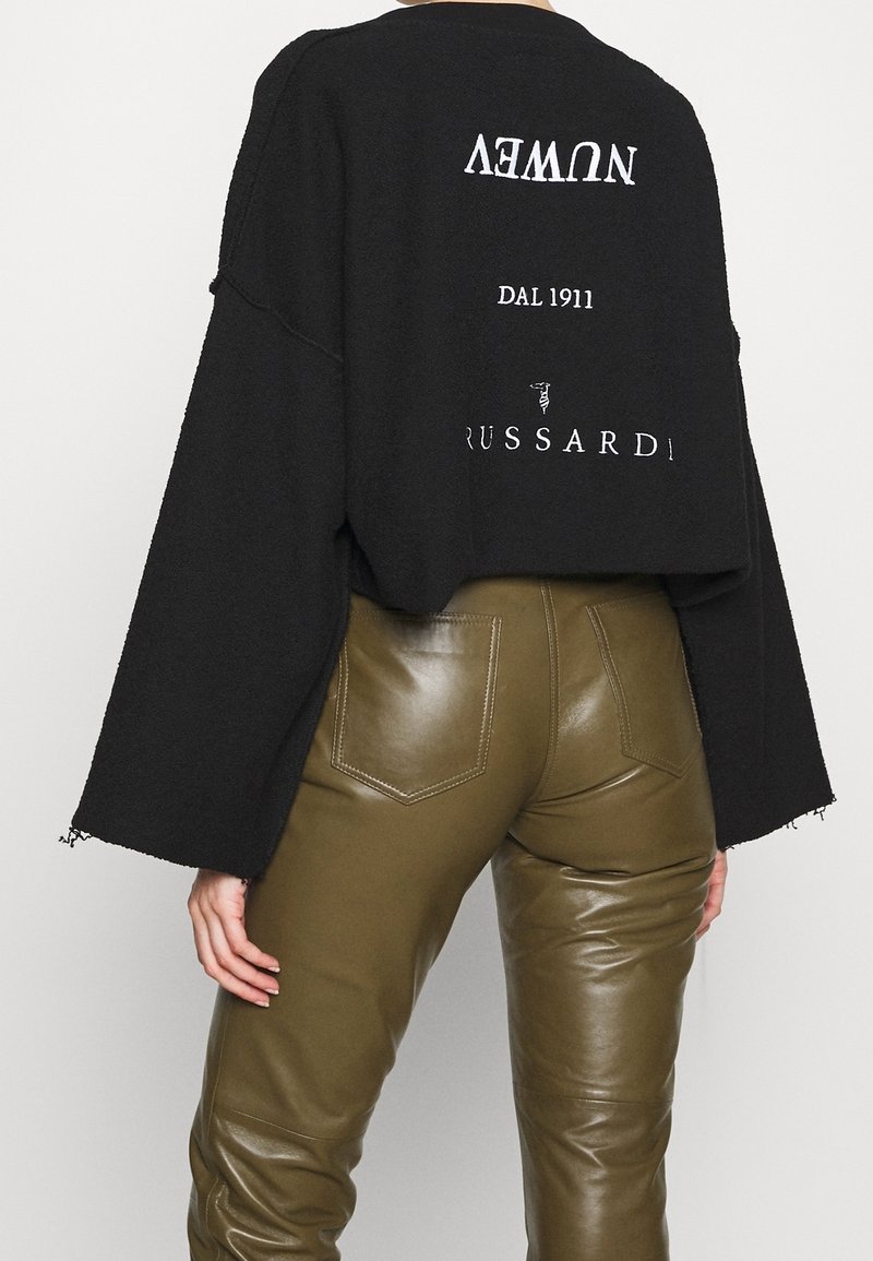 Sweat-shirt noir court à manches larges, avec texte et logos blancs. Associé à un pantalon slim vert olive en simili cuir avec poches.