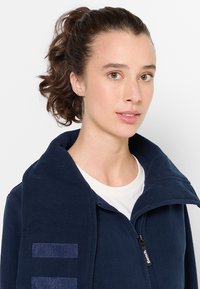 Giacca in pile blu navy con colletto alto, zip frontale e dettagli in denim. Caratterizzata da una texture liscia e un design casual.