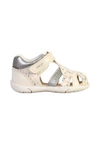 Sandalia blanca hecha de material flexible, con un diseño de cortes, acentos metálicos plateados y patrones florales. Cierre con tira de velcro.