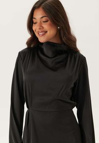 Abito in satin nero con collo alto, maniche lunghe e un design fluido e morbido con una vita aderente.