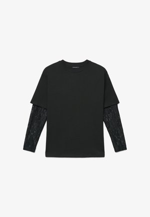 Camicia nera a maniche corte con maniche lunghe in pizzo abbinato, collo tondo, distesa su sfondo bianco.