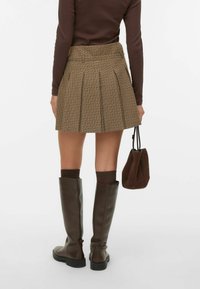 Bruine geruite plooirok met hoge taille, gecombineerd met kniehoge bruine leren laarzen en een bruine rugzak met trekkoord.