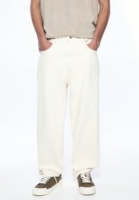 White denim wide-leg pants with visible stitching, side pockets, worn with olive green sneakers featuring white laces and a thick sole.