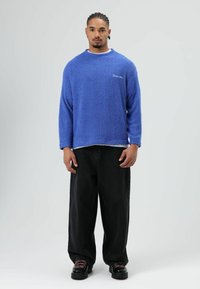 Blauwe, zachtgevoerde trui met een ronde hals, lange mouwen en een gestikte zoom, gecombineerd met losse zwarte spijkerbroek en robuuste zwarte schoenen.