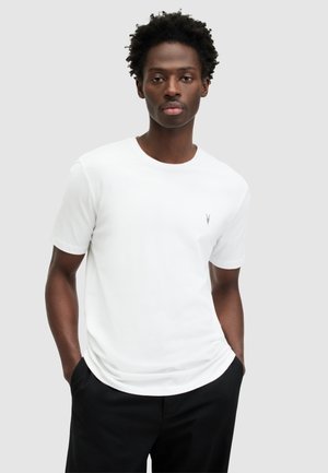 Hvid bomulds t-shirt med rund halsudskæring og korte ærmer, med et lille gråt logo på brystet, parret med mørke bukser.