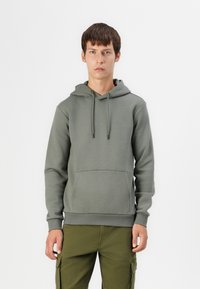 Olive green cotton hoodie with a front pocket, drawstring hood, and ribbed cuffs. Worn with cargo pants. Simple, minimalist design.