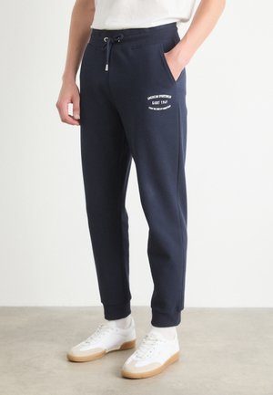 Navy blue sweatpants made of soft material, featuring cuffs, drawstring waist, and side pockets. Includes white logo detail on the front.
