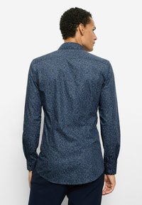 Marineblaue Langarmbluse mit einem verstreuten hellblauen und weißen Muster, Knopfleiste am Kragen und tailliertem Schnitt. Mit knöpfbaren Manschetten.