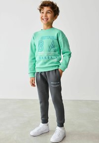 Mintgrön sweatshirt med blå text, parat med grå mjukbyxor. Outfiten har ribbade mudd och vita sneakers.