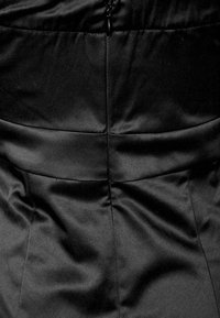 Svart satinklänning med en åtsittande baksida med subtila sömmar och en dold dragkedja, som visar en mjuk, glänsande yta.