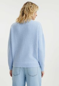 Hellblauer gestrickter Pullover mit entspannter Passform, abgesenkten Schultern und geripptem Saum. Weicher Stoff, kombiniert mit hellblauen Jeans.
