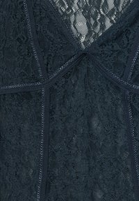 Nahaufnahme von schwarzer Spitzenstoff mit aufwendigen Blumenmustern und vertikalen Nähdetails.