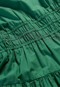 Grön bomullstyg med samlingsdetaljer, som har flera sydda elastiska sektioner som skapar en texturerad, rufsig look.