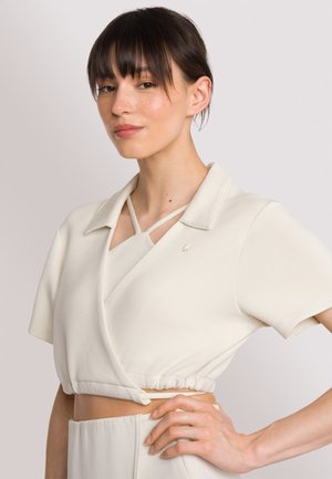 Witte cropped top met een wikkelontwerp, korte mouwen en een ronde kraag; heeft gekruiste bandjes bij de halslijn en een elastische taille.