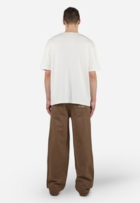 White short-sleeve shirt with a straight cut, paired with loose-fitting brown pants featuring back pockets and subtle stitching details.