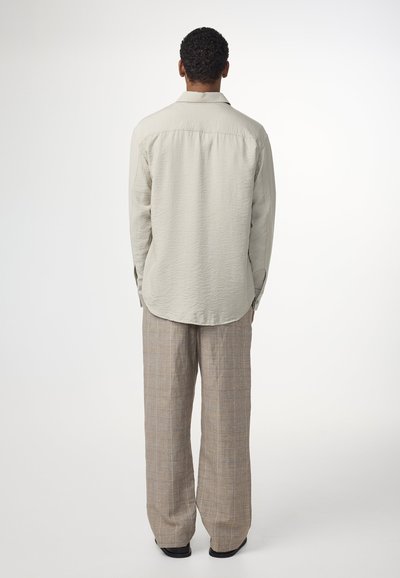 Ljusgrå långärmad skjorta med texturerad yta, tillsammans med lösa rutiga byxor i beige och bruna toner.