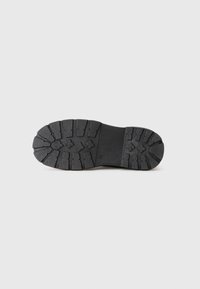 Suela de goma negra de un zapato con patrones de relieve profundos y el número 37 estampado en el centro, fotografiado sobre fondo blanco.