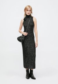 Long black knit dress with a high neck, embellished with silver flecks, paired with black ankle boots and a small black handbag.
